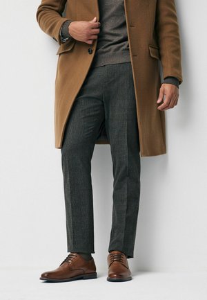 Brown wool coat over a gray sweater, paired with gray checkered pants and brown leather shoes. Textured fabric and tailored fit details visible.