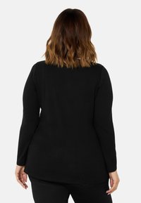 Mustapaitainen pitkähiha, jossa on kaareva helma, sileä kangas ja rento istuvuus. Takakuvasta näkyy yksinkertainen muotoilu ilman koristelua.