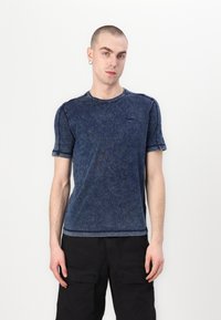 Tricou din bumbac de culoare bleu închis, cu mânecă scurtă și gât rotund, având o textură subtilă, prezentând co stitching în nuanță de albastru și un mic detaliu cu logo pe piept.