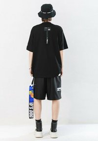 Camiseta negra de gran tamaño con mangas cortas y una etiqueta en la parte de atrás, combinada con pantalones cortos negros y botas cortas negras. Una bolsa cuelga de la cintura.
