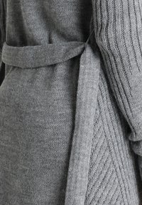 Šedý pletený kardigan s texturovaným vzorem, s páskem na vázání v pase a žebrovanými rukávy pro větší detail a strukturu.