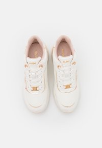 Baskets blanches avec doublure intérieure rose, accents dorés et broderie florale, vues de dessus sur un fond clair.