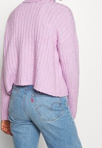 Lilak geribde trui met een cropped design, gecombineerd met lichtblauwe denim jeans. Opvallende stiksels op de achterzakken van de jeans.