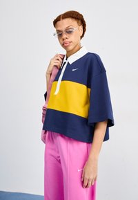 Donkerblauwe, gele en witte kleurgeblokte poloshirt met een relaxte pasvorm en korte mouwen, gecombineerd met roze trainingsbroeken.