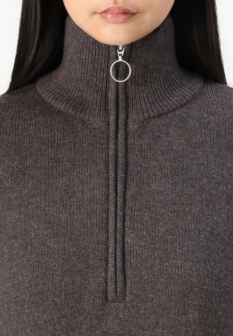 Brauner Strickpullover mit hohem Kragen, ausgestattet mit einem Halb-Reißverschluss und einem runden Reißverschlussanhänger zum Schließen. Weiche Textur und taillierte Passform.