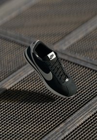 Sort Nike sneaker med grå accenter, materialer af ruskind og mesh, struktureret sål, smal form og klassisk snørebåndsdesign.