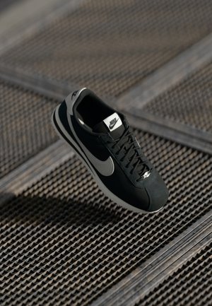 Black Nike sneaker with grey accents, suede and mesh materials, textured sole, narrow shape, and classic lace-up design.