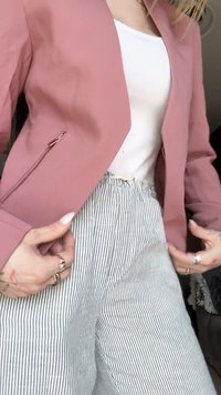 Rožinė blazer su užtrauktuku ir balta palaidine, derinama su dryžuotomis plačiomis kelnėmis, turinčiomis elastinį juosmenį.