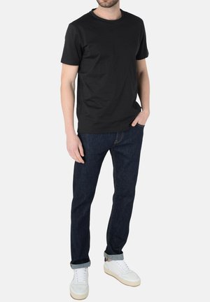 T-shirt nera in cotone, colletto rotondo, indossata con jeans in denim scuro e sneakers bianche. Design semplice con vestibilità slim, senza modelli o loghi visibili.