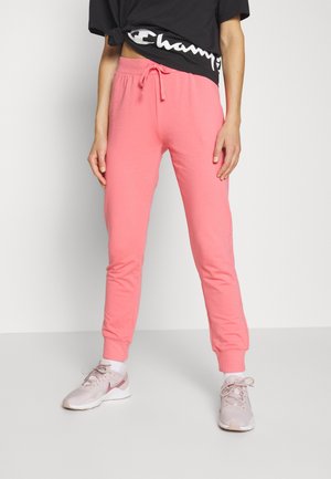 Pantalons de jogging roses avec une taille à cordon, des poignets aux chevilles et une texture douce, associés avec des baskets de teintes neutres et un crop top noir.