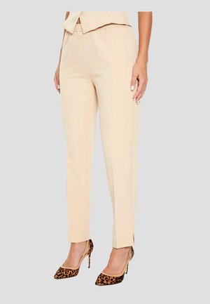 Beige tailored pants with an elastic waistband, side slits at the ankles, paired with leopard-print high heels on a gray background.