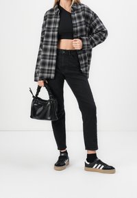 Svart och vit rutmönstrad skjorta med knappar, svart croppad topp, svarta jeans, svarta sneakers med vita ränder, och en liten texturerad svart väska.