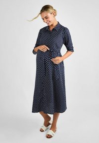 Tummansininen midi-mekko valkoisilla pallokuoseilla, kauluksellinen pääntie, ¾-pituiset hihat ja vyötäröllä säädettävä vyö.