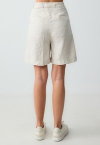 Shorts en lin beiges avec une taille mi-haute, des jambes larges et deux poches arrière. L'ourlet est légèrement courbé. Associés à des baskets blanches.