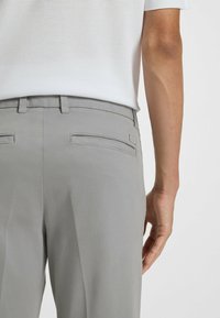 Pantaloni grigi con una texture liscia, dotati di due tasche posteriori, cuciture sottili e un'etichetta con il marchio vicino alla tasca destra.