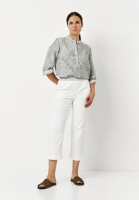 Lichtblauw patroon blouse met korte mouwen, gecombineerd met witte cropped broek en bruine gevlochten schuifsandalen. Schoon, casual uiterlijk.