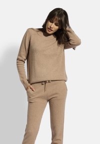 Suéter de punto beige con cuello redondo y mangas largas, combinado con pantalones de ajuste por cordón a juego. Textura suave, corte relajado, diseño minimalista.