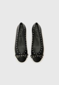 Black leather ballet flats featuring a rounded toe, decorative metal eyelets around the edge, and a bow accent on the toe.