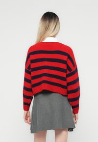 Rød og marineblå stripete strikkegenser med lange, vide ermer og kort snitt, kombinert med en grå svingekjole. Myk tekstur synlig.
