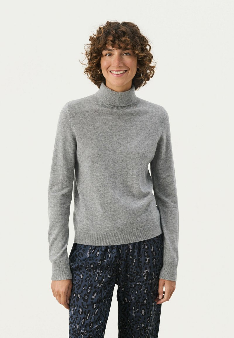 Grauer Rollkragenpullover mit langen Ärmeln, aus weichem Material, mit gerippten Bündchen und Saum, kombiniert mit gemusterten, dunklen Hosen.