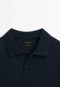 Polo bleu marine en tissu texturé, avec un col classique, une patte de boutonnage à deux boutons et une étiquette de marque cousue à l'intérieur.