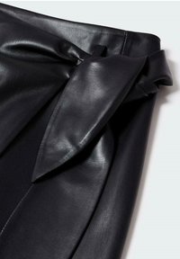Jupe en cuir noir avec une large taille et un détail de nœud décoratif, texture lisse et plis structurés.