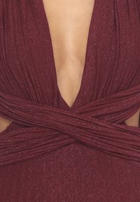 Abito bordeaux con scollatura a V profonda, tessuto drappeggiato e sparkle testurizzati. Presenta dettagli attorcigliati in vida.