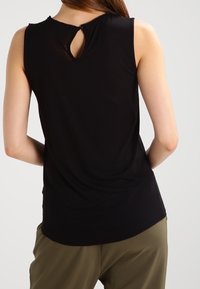 Haut sans manches noir avec une découpe en forme de serrure au dos, ourlet arrondi et texture de tissu lisse. Assorti à un pantalon vert olive.