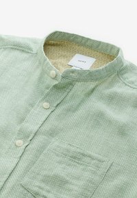 Camisa verde claro con cuello, hecha de una tela texturizada, que cuenta con un bolsillo de parche y cuatro botones blancos, con un forro interior estampado.