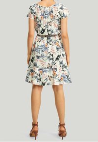 Robe fleurie à manches courtes, avec un col froncé et une taille cintrée. Le tissu a une texture légère et fluide avec un fond pastel.