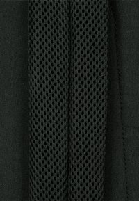 Svart tyg med ett texturerat nätpanel, med små cirkulära öppningar, vid sidan av slätt material, som kontrasterar i yta och design.