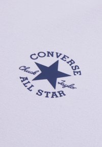 Bílá tkanina s tmavě modrým hvězdným logem a textem „CONVERSE ALL STAR“ a „Chuck Taylor“ v kruhovém designu.