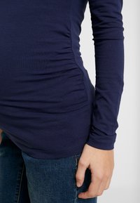 Marinblå långärmad topp i mjukt tyg. Har rynkad detalj vid sidan, matchad med blå denimjeans. Strukturerad, avslappnad design.