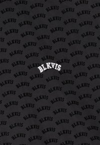 Tissu noir présentant un motif répétitif du texte "BLKVIS" dans différentes nuances de noir. Le logo central est en blanc.