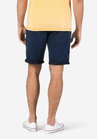 Navy blue shorts with rolled cuffs, made from a smooth material. Worn with white low-top sneakers and a light yellow shirt.