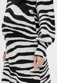 Knit svetr s černobílým pruhem, který má uvolněný střih, dlouhé rukávy a široké manžety. Je vyroben z jemného materiálu s mírným strečem.