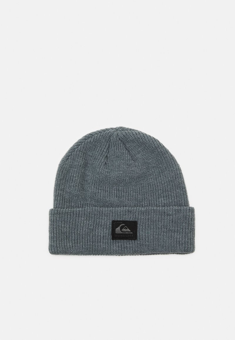 Grå stickad beanie med en vikbar kant, med en svart etikett som har en vit bergslogotyp. Materialet verkar mjukt och texturerat.