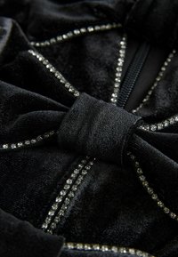 Black fabric with a soft texture features a prominent bow detail. Accents of small, shiny rhinestones highlight the edges and seams.