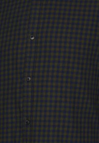 Camicia a quadri in verde scuro e blu navy, realizzata in cotone. Presenta bottoni e colletto standard, con una texture liscia e una vestibilità regolare.