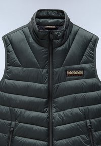 Vadderad mörkgrön väst med hög krage, med en central dragkedja och sidofickor. Inkluderar en logotyp-patch på vänster bröstområde.