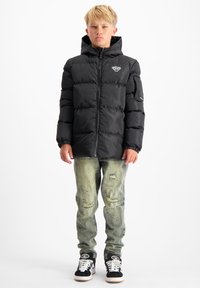 Zwarte gewatteerde jas met ritssluiting en capuchon, met een logo op de borst, gecombineerd met versleten lichte denim jeans en zwarte sneakers.