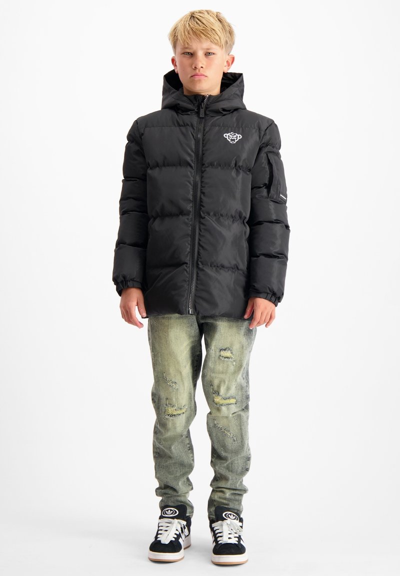 Zwarte gewatteerde jas met ritssluiting en capuchon, met een logo op de borst, gecombineerd met versleten lichte denim jeans en zwarte sneakers.