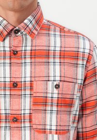 Camicia a quadri rossa e bianca con dettagli neri, dotata di taschino sul petto e colletto classico. Tessuto texturizzato.
