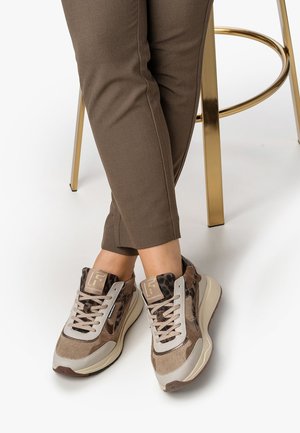 Sneaker leopardati marroni e beige con lacci, indossati con pantaloni marroni, piedi incrociati mentre si è seduti su uno sgabello di metallo dorato.
