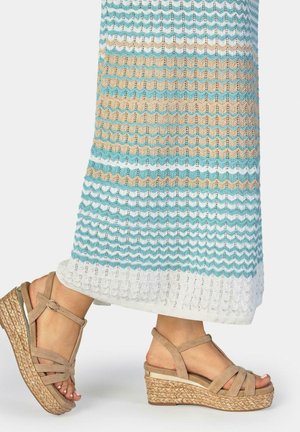 Pies con sandalias cuña beige de tiras con suelas trenzadas, combinados con una falda larga de punto con patrones en zigzag azul, beige y blanco.