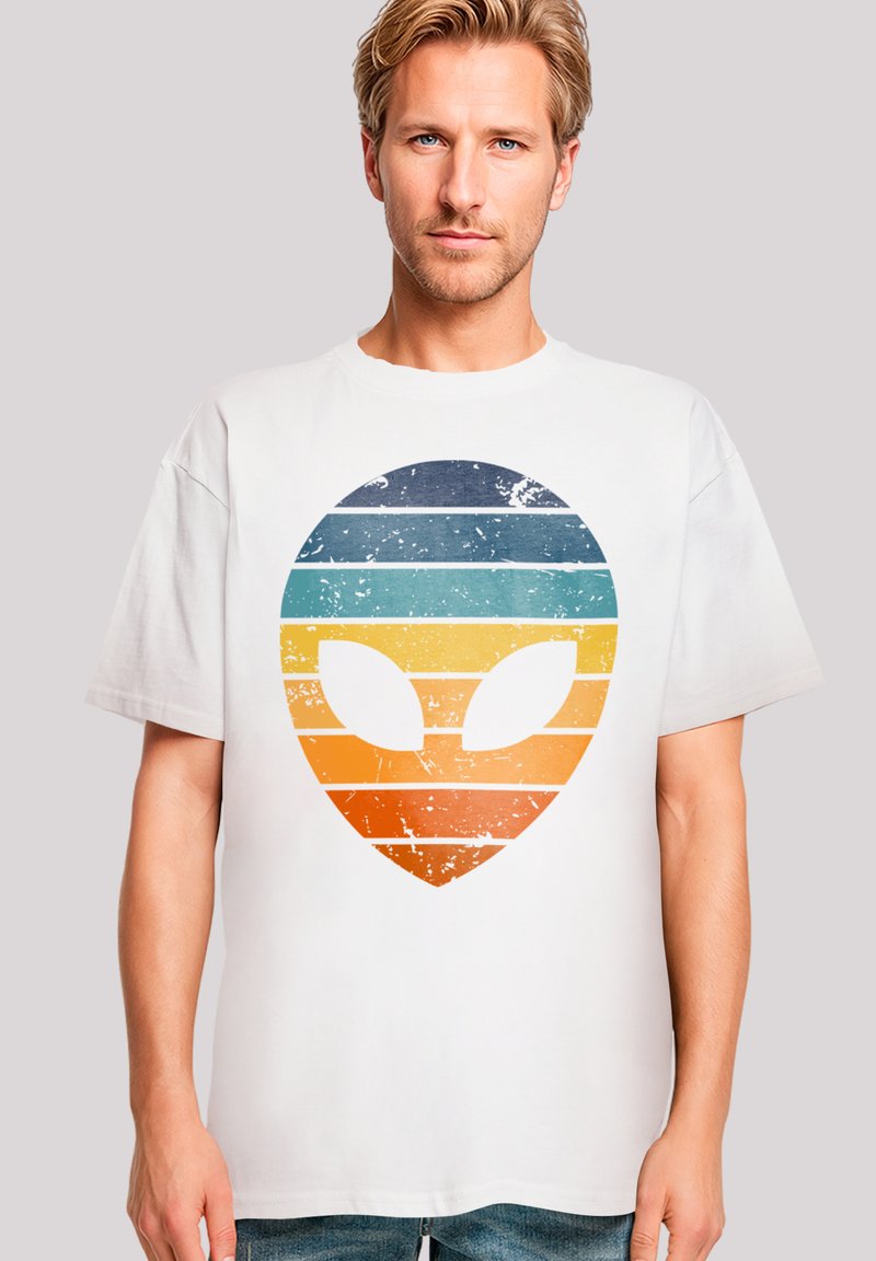 White short-sleeve t-shirt featuring a retro alien graphic with horizontal blue, teal, yellow, and orange stripes, and distressed detailing.