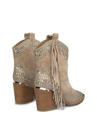 Botas de tobillo de ante beige con flecos, acentos metálicos y recortes decorativos; tacón de madera apilado; punta afilada.