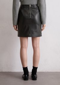 Zwarte leren minirok met een rits aan de voorkant, een gladde textuur en een aansluitend ontwerp, gecombineerd met zwarte sokken en loafers.