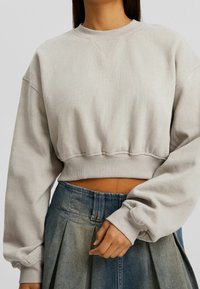 Sudadera recortada de tejido gris claro con cuello y puños acanalados, con un ajuste holgado y hombros caídos, combinada con una falda de mezclilla.