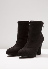 Bottes basses en daim noir avec un talon bloc haut, design sans coutures, bout arrondi, et une languette à l'arrière. Texture lisse dans l'ensemble.